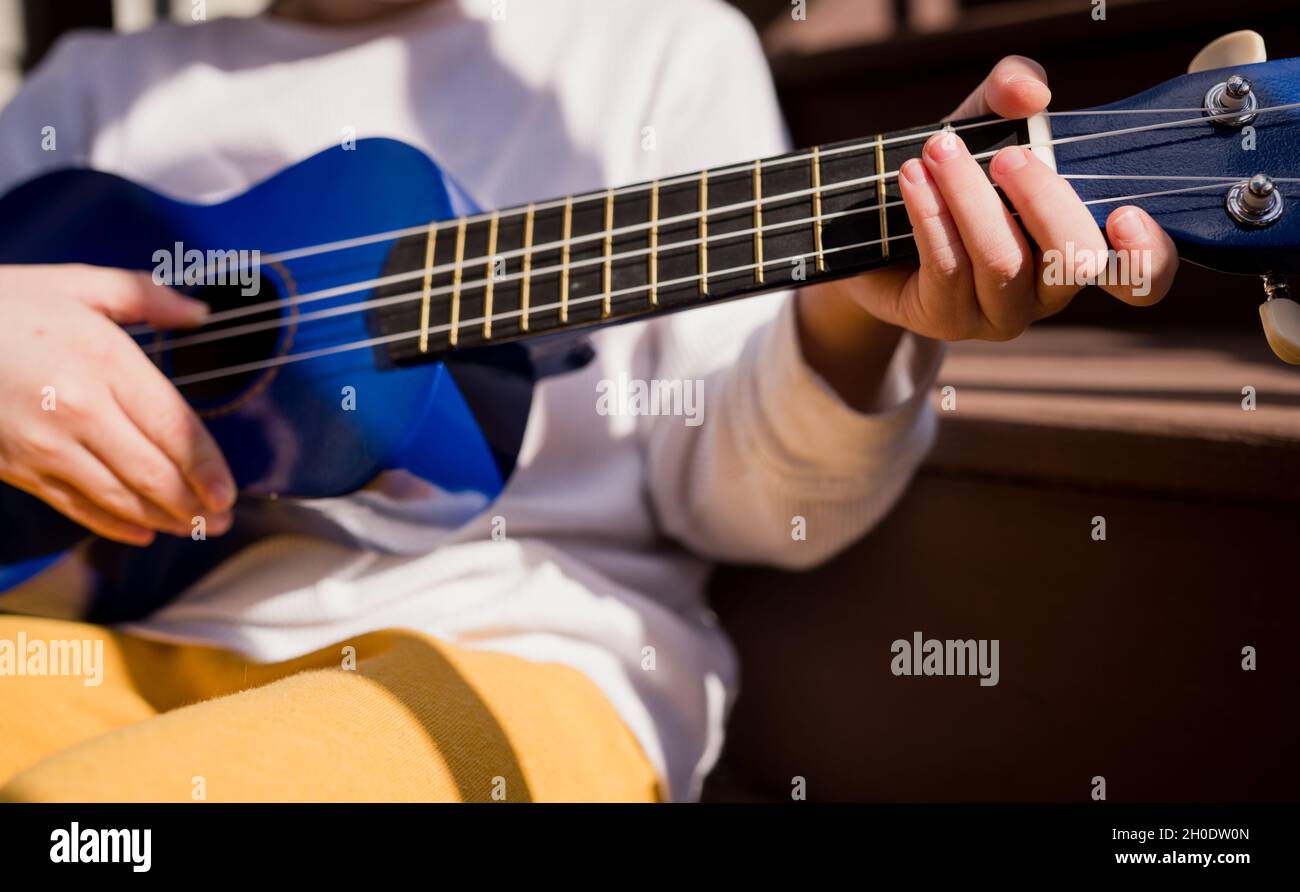 Kleiner Junge, der im Sonnenschein die Ukulele spielt Stockfoto