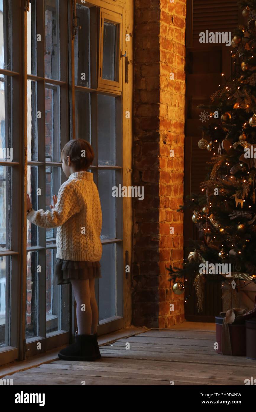 Das Kind schaut aus dem Fenster an heiligabend von der Seite. Stockfoto
