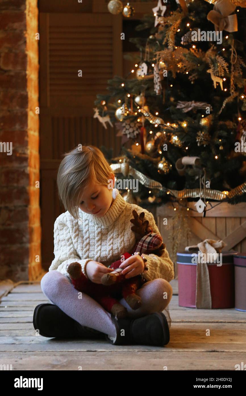 Das Kind umarmt ein weiches Spielzeug, während es in warmen Kleidern sitzt. Stockfoto