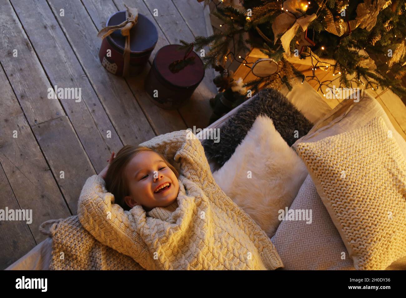 Lächelndes Kind liegt auf dem Bett in der Nähe des weihnachtsbaums von oben. Stockfoto