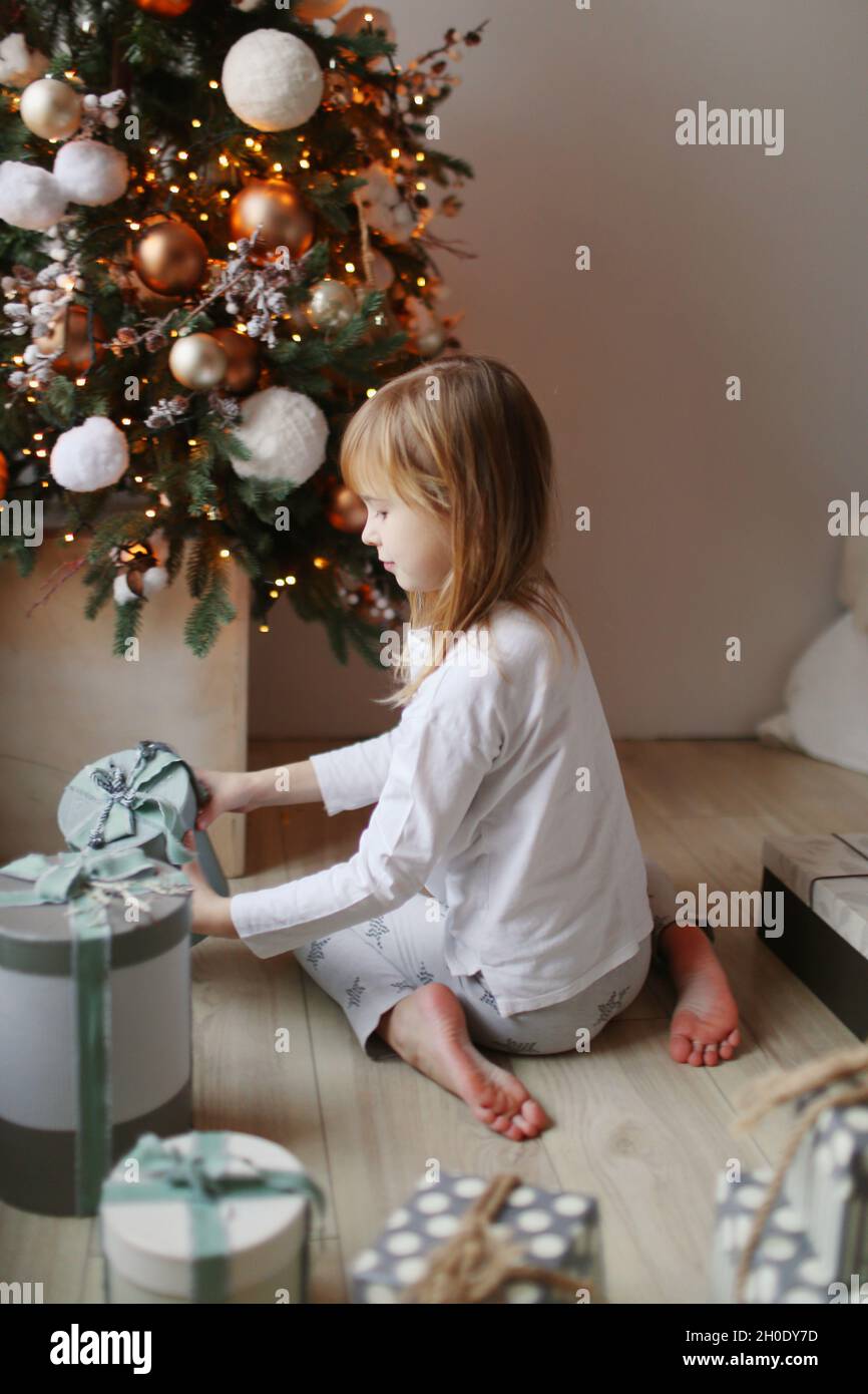 Mädchen, das auf dem Boden sitzt und Geschenke in der Nähe des weihnachtsbaums hat Stockfoto