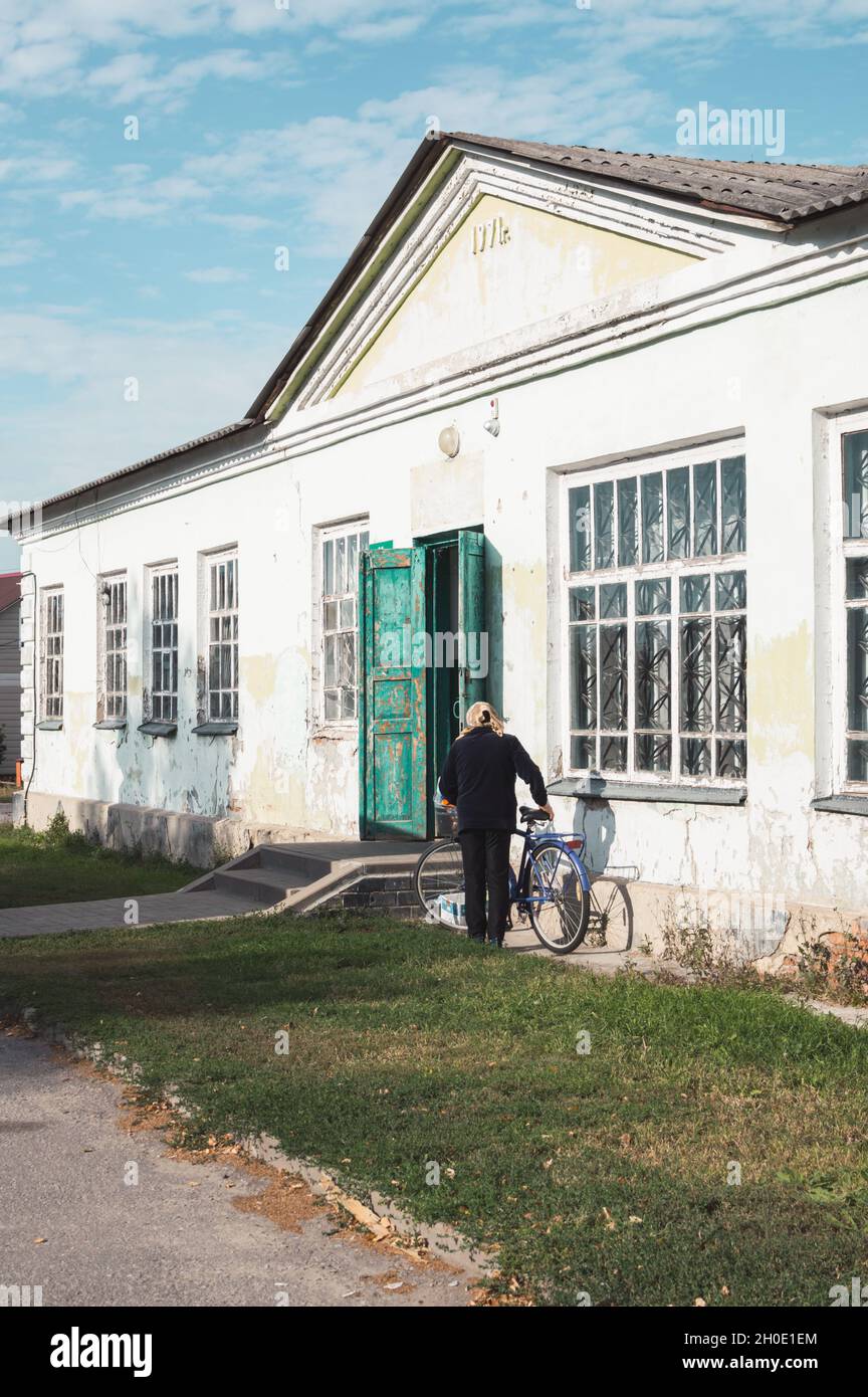 Eine Frau steigt auf ein Fahrrad neben einem alten, abblätternden Vintage-Gebäude aus dem Jahr 1971 Stockfoto