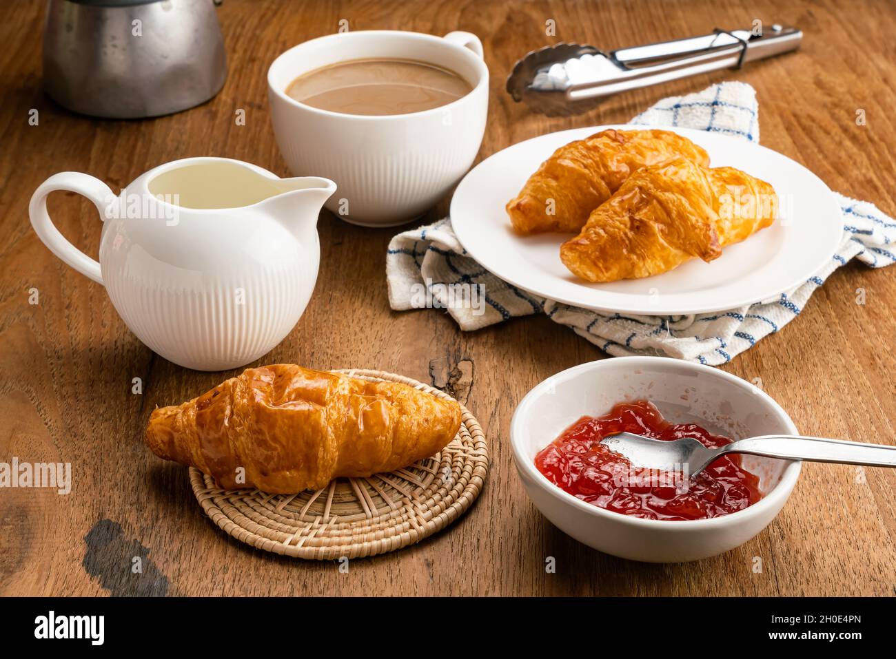 Frühstück mit leckeren hausgemachten Croissants, Erdbeermarmelade und heißem Milchkaffee. Frisch gebackene Croissants in weißer Keramikschale mit Erdbeermarmelade Stockfoto