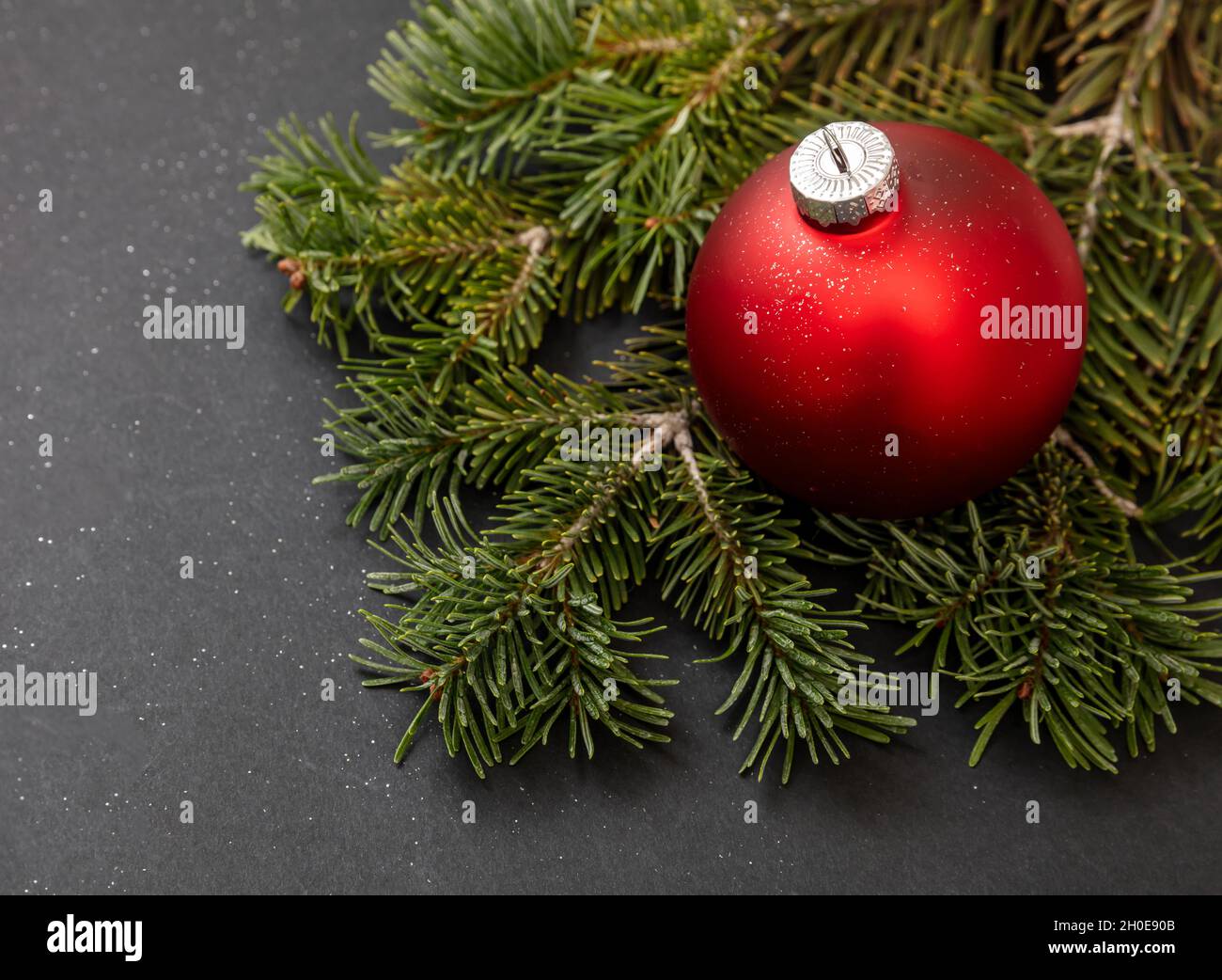 Weihnachtsdekoration. Rote Weihnachtskugel und frischer Tannenzweig auf schwarzem Hintergrund, Winterurlaub-Dekor, Nahaufnahme. Stockfoto