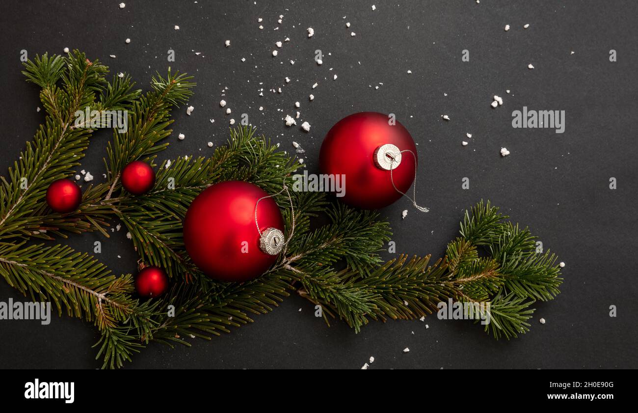 Weihnachtsdekoration. Rote Weihnachtskugeln und frischer Tannenzweig auf schwarzem Hintergrund, Einrichtung für Winterferien, Nahaufnahme. Stockfoto