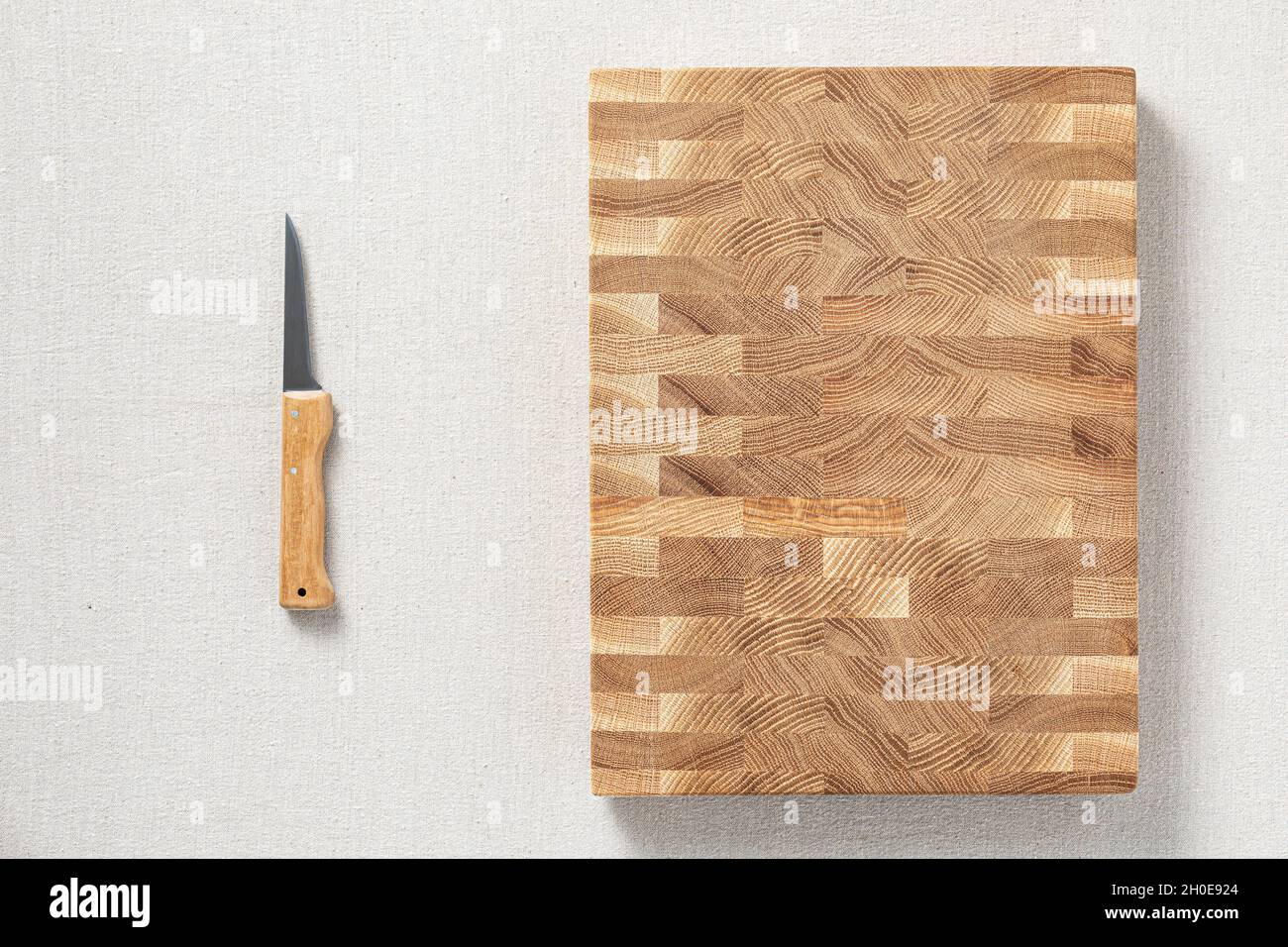Ein Messer und eine Eiche gespleißt ​​wooden Schneidebrett sind auf Sackleinen. Der Querschnitt der Eichendiele hat eine Mosaikstruktur. Hintergrundelement. Stockfoto
