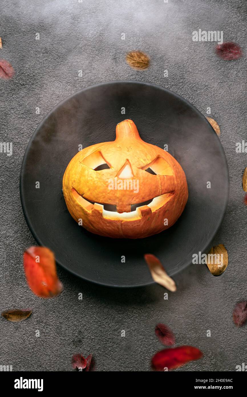 Ein gruseliger orangefarbener Kürbis auf dem Tisch, leuchtende Augen, ein schwarzer Teller und ein Hintergrund. halloween Party Einladung in ein Restaurant oder zu einer Feier in einem Stockfoto