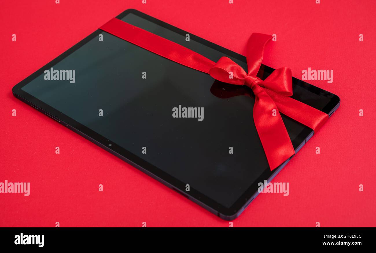 Digitales Tablet Weihnachtsgeschenk auf rotem Hintergrund. Elektronisches Gerät mit rotem Band Schleife gebunden. Valentinstag, Weihnachten Urlaub Geschenk. Stockfoto