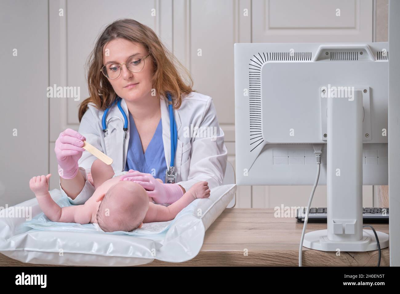 Der Arzt untersucht den Hals eines neugeborenen Kindes mit Pflugschare.  Eine Krankenschwester in Uniform mit einem Holzstab in der Hand untersucht  den Kindermund Stockfotografie - Alamy