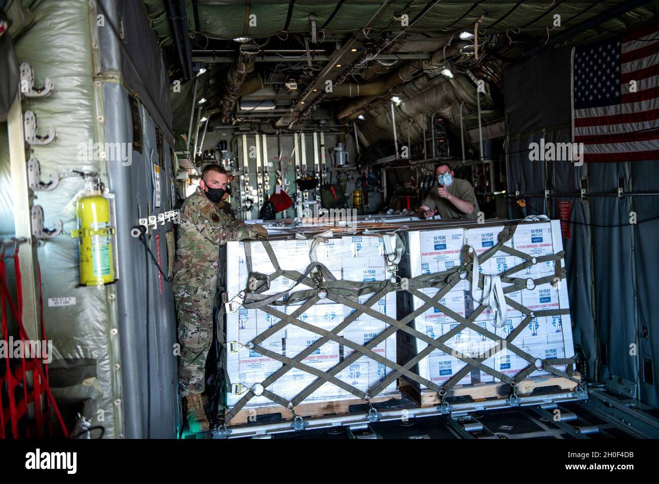 Die US Air Force Airmen unterstützen die Koordination und das Entladen von abgefülltem Wasser auf einer C-130 vom 136. Airlift Wing, Texas Air National Guard, Ft. Worth, 21. Februar 2021, bei der Joint Base San Antonio-Kelly Field, Texas. Das 502. Logistics Readiness Squadron unterstützte die Koordination und das Entladen von etwa 80,000 Flaschen Wasser, die über Flugzeuge auf dem Kelly Field eingeliefert wurden und nach dem Wintersturm Uri an die Stadt San Antonio verteilt werden sollten. Stockfoto