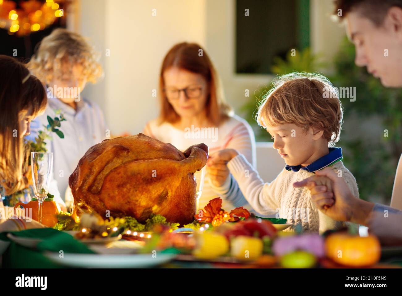 Familie am Thanksgiving-Abendessen. Eltern, Großeltern und Kinder genießen geröstete pute- und Gemüsemahlzeiten. Kinder und Großmutter sagen ein dankbares Gebet. Stockfoto