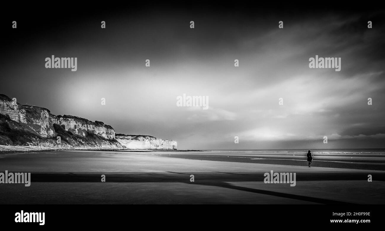 Schwarz-Weiß-Bild von Einzelfigur am Strand von Utah Normandie Frankreich. Mit Klippen, Strand, Meer und herrlichem Himmel. Stockfoto