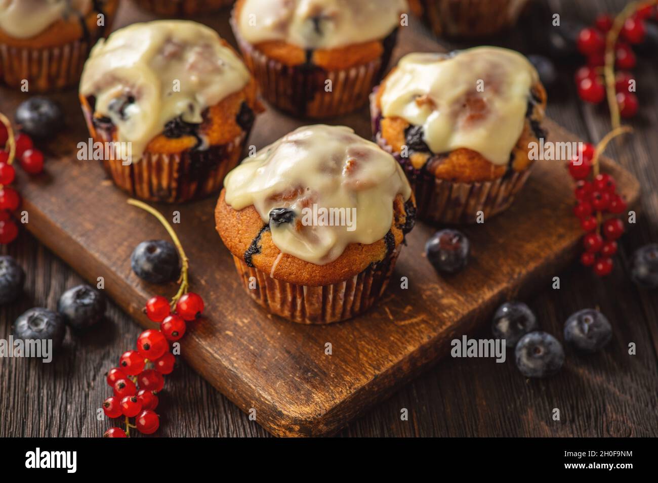 Hausgemachte Muffins mit roten Johannisbeeren und Blaubeeren, bedeckt mit weißer Schokolade. Stockfoto