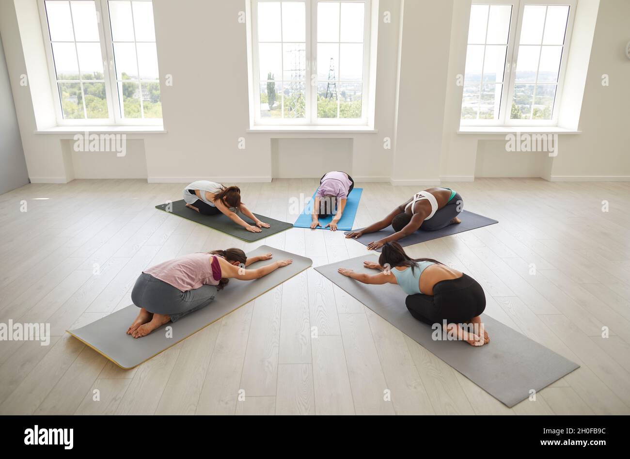 Verschiedene junge Frauen üben gemeinsam Yoga in einer Gruppensitzung in einem hellen, geräumigen Raum. Stockfoto