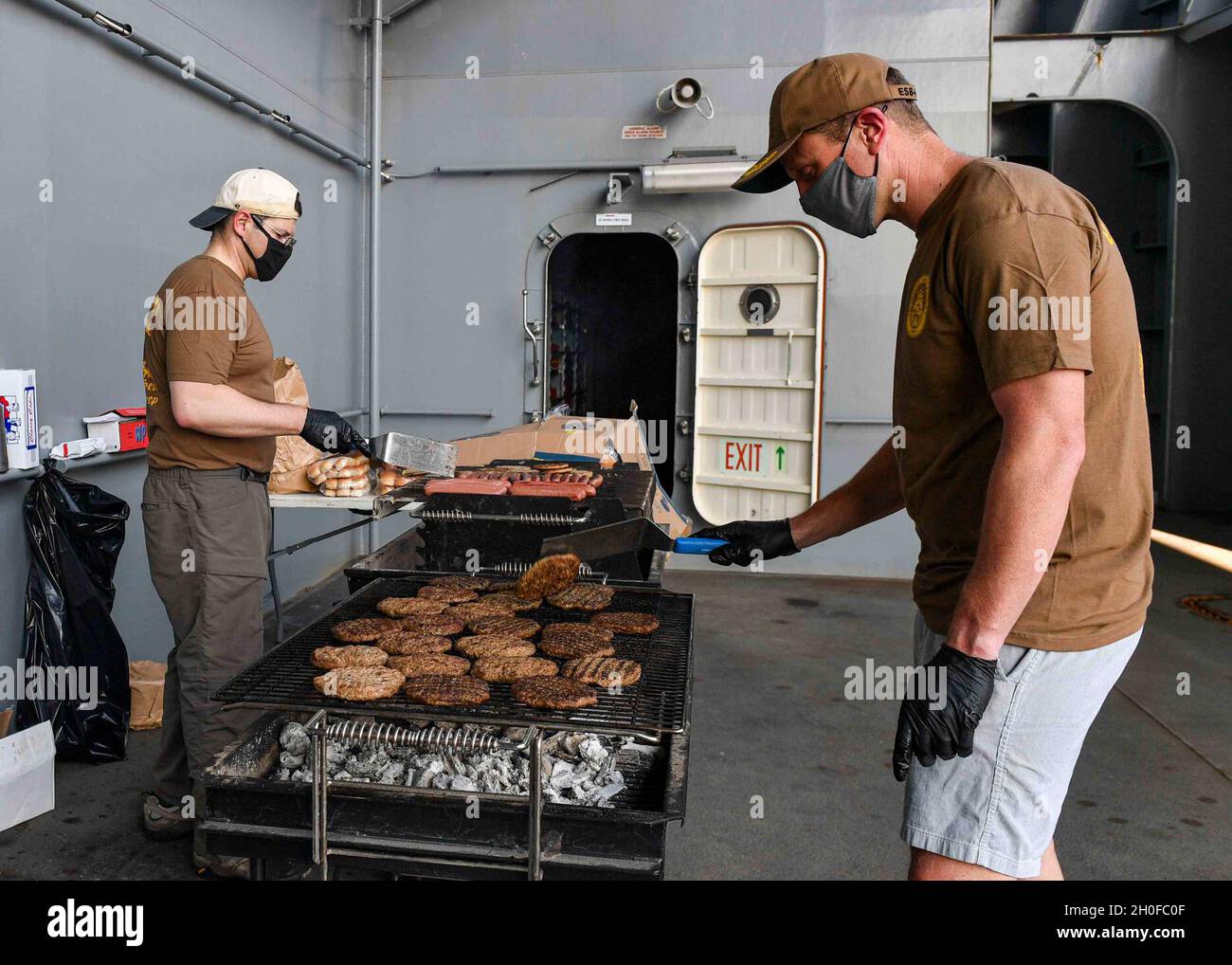 KAPSTADT, Südafrika (Feb 24, 2021) Bef. Joseph Fitzpatrick, links, und cmd. Jeffery Moore grillen auf dem Missionsdeck während eines „Steel Beach“-Picknicks an Bord der Expeditionary Sea Base USS Hershel „Woody“ Williams (ESB 4) in Kapstadt, Südafrika, 24. Februar 2021. Hershel „Woody“ Williams ist in der sechsten US-Flotte tätig, um Interoperabilitätsschulungen durchzuführen und strategische Partnerschaften mit ihren afrikanischen Partnern aufzubauen. Stockfoto