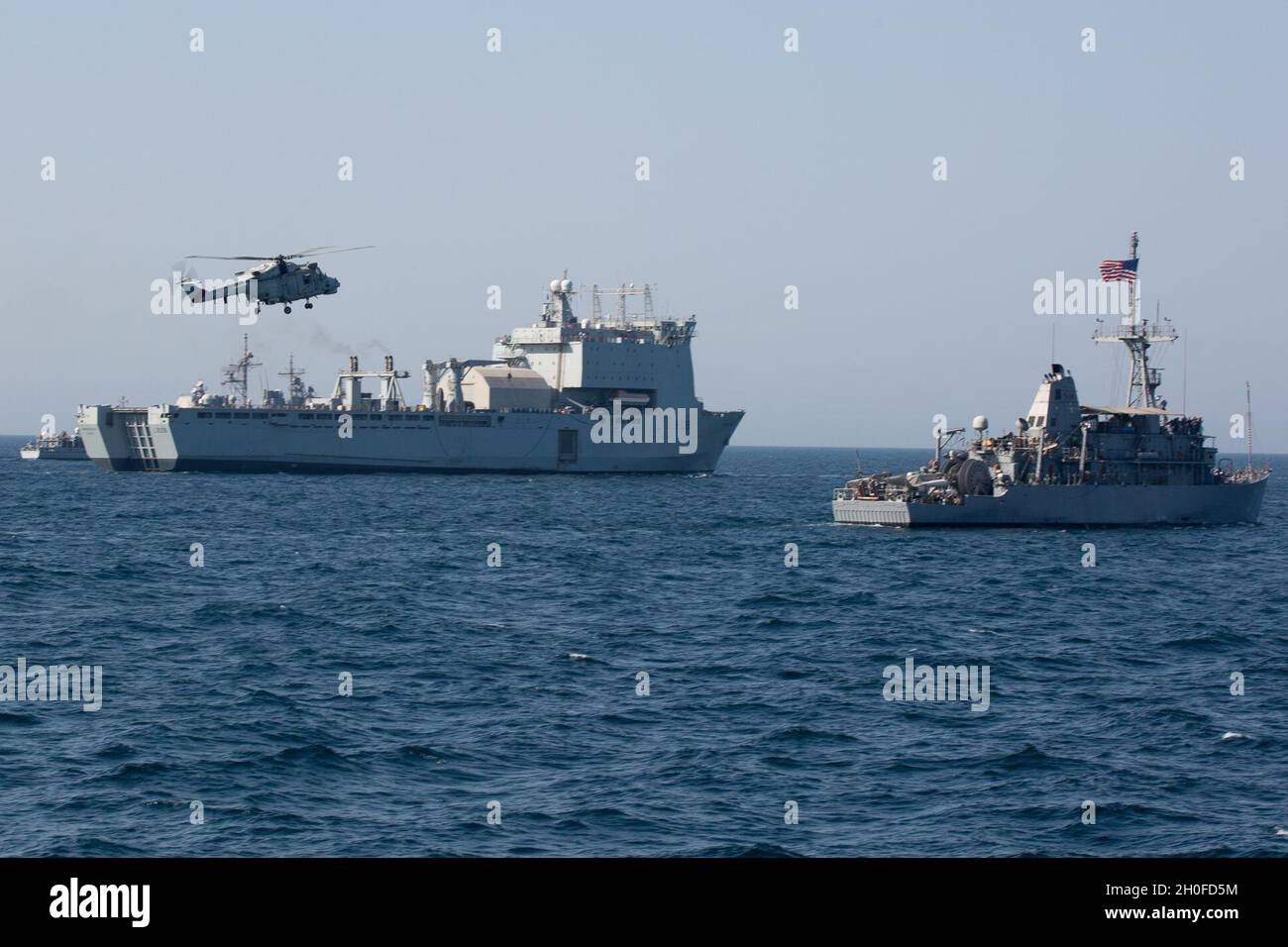 210224-A-BD272-0980 SEA OF OMAN (FEB 24, 2021) - Ein Hubschrauber der Royal Navy of Oman Lynx operiert in Formation mit Landeanlegestelle RFA Cardigan Bay (L 3009), links und Minengegenmaßnahmen Schiff USS Sentry (MCM 3) während der Koalitionsübung Khunjar Hadd 26 im Oman-Meer, 24. Februar. Khunjar Hadd 26 ist eine jährliche Übung zur Verbesserung der gegenseitigen maritimen Fähigkeiten und der Interoperabilität zwischen den US-, omanischen, französischen und britischen Militärkräften, um Bedrohungen für die Freiheit der Navigation und den freien Fluss des internationalen Handels anzugehen. Stockfoto