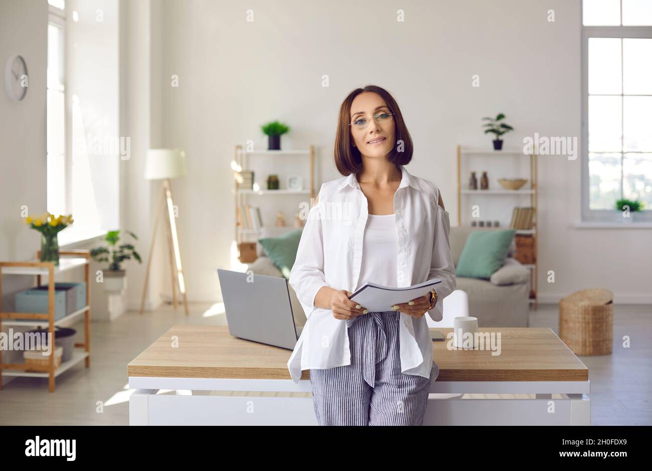 Porträt einer eleganten erwachsenen Geschäftsfrau, die am Schreibtisch in ihrem Heimbüro steht Stockfoto