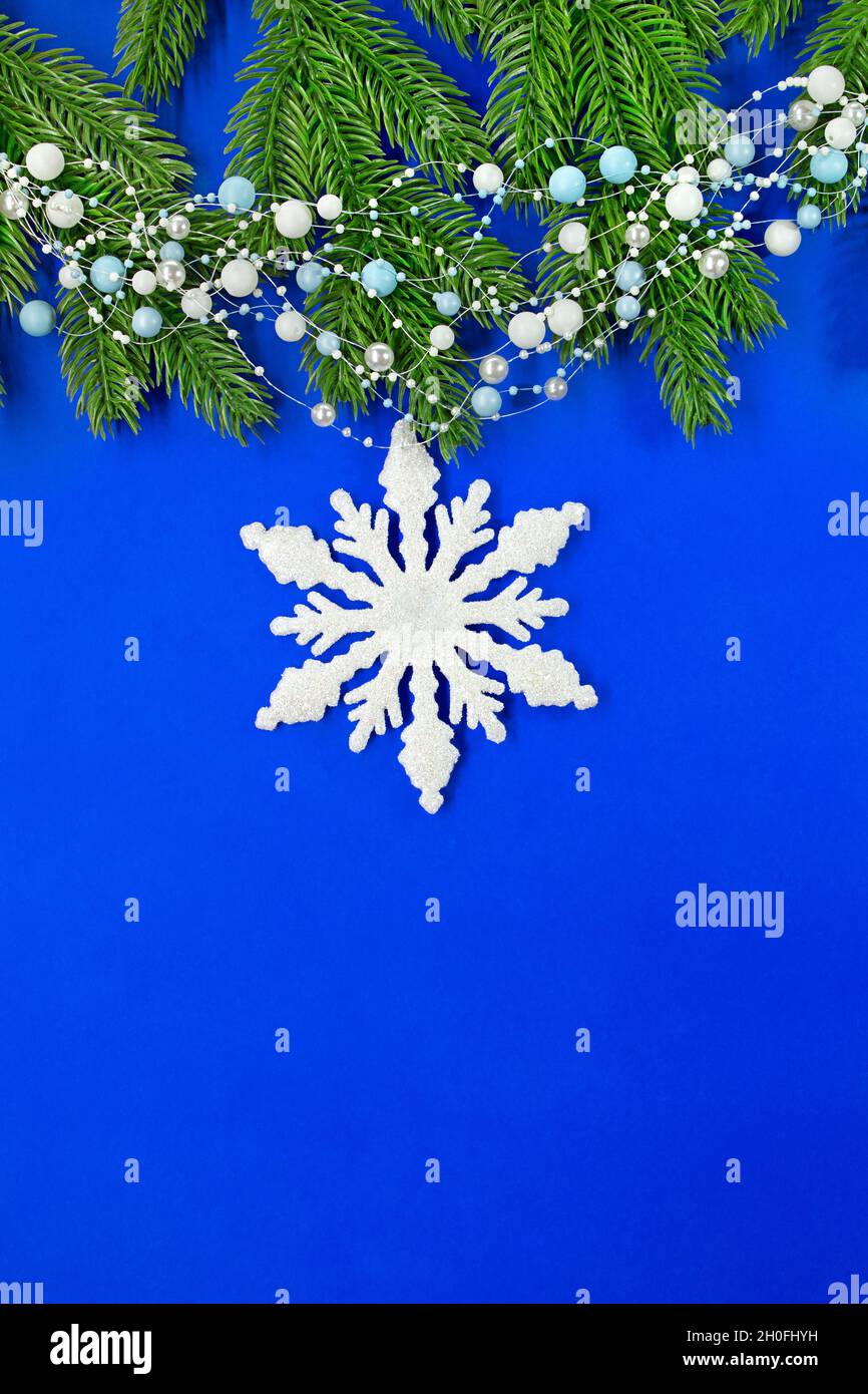 Weihnachtsbaum Äste mit Girlande aus Perlen und Schneeflocke auf blauem Hintergrund. Weihnachten und Neujahr Hintergrund. Vertikal. Speicherplatz kopieren Stockfoto