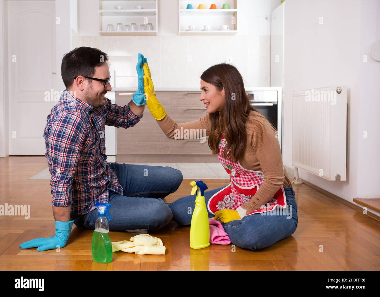 Ein glückliches junges Paar, das nach dem Housekeeping auf dem Boden saß und mir fünf Gesten gab Stockfoto