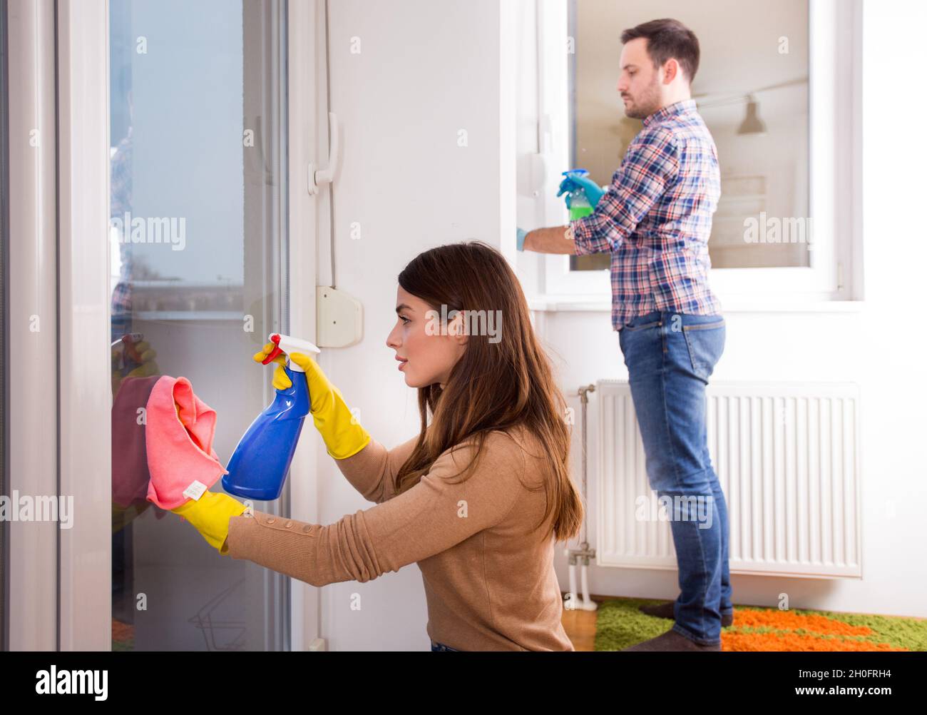 Mann und Frau putzen Fenster mit Tuch und Sprühflasche zu Hause Stockfoto