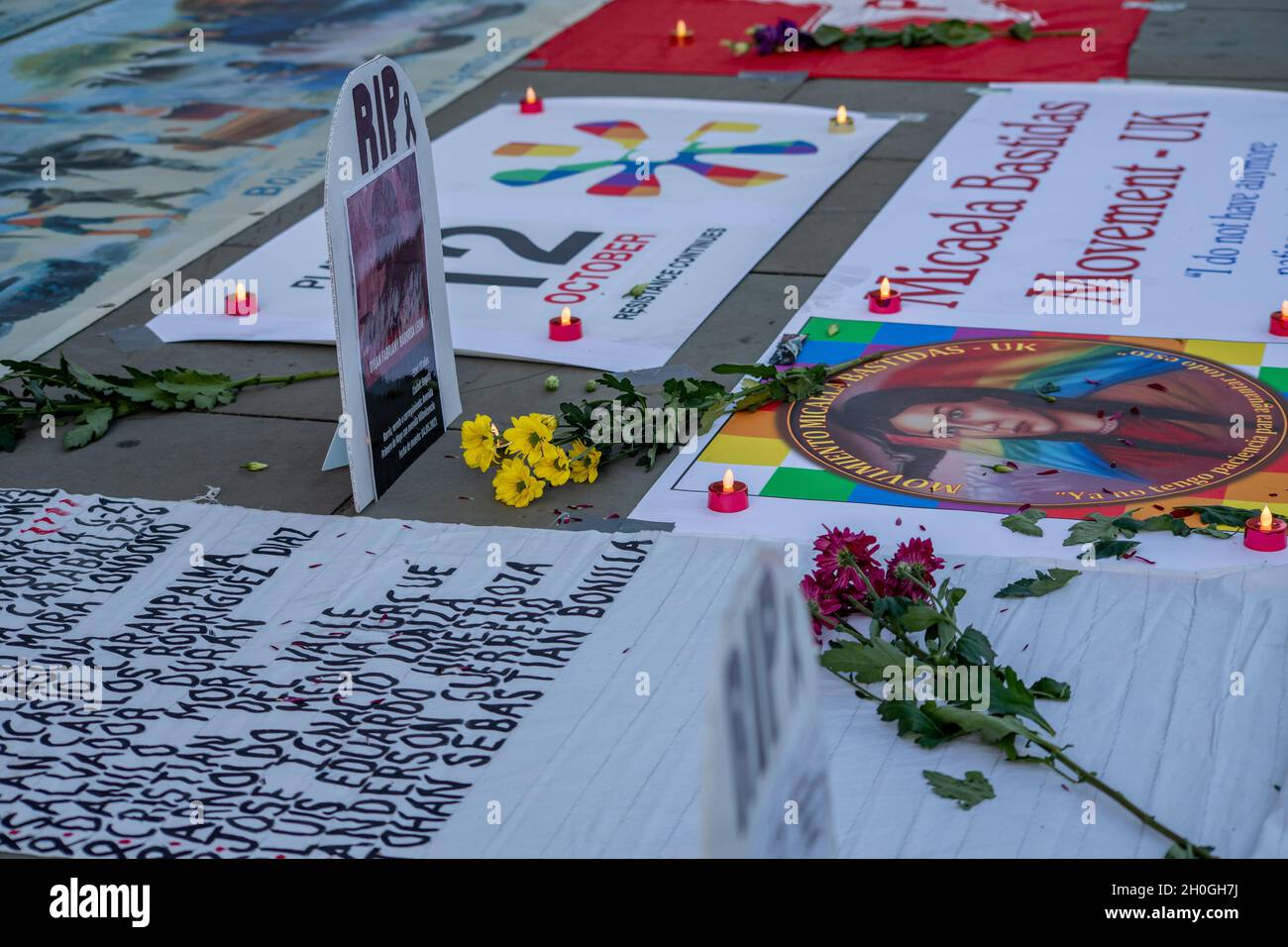 Trafalgar Square, London, England, Großbritannien 12. Oktober 2021 Columbus muss fallen! Neokolonialismus Muss Fallen! Indigene Völker protestieren gegen die Feier von Kolumbus. Symbolische Grabsteine mit den Namen und Bildern der Verstorbenen wurden auf dem Boden vor der Nationalgalerie aufgestellt, geschmückt mit Blumen und Kerzen. Im Anschluss an die Reden gab es eine Aufführung von Tänzern in indigenen Kostümen. Stockfoto