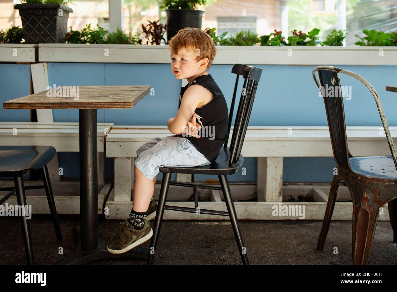 Essen im Freien während der Covid 19. Ein kleiner Junge, der an einem leeren Tisch in einem Restaurant in New York City sitzt. Stockfoto