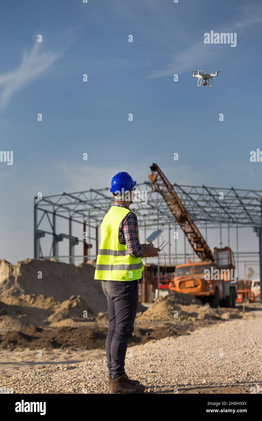 Rückansicht des Ingenieurs, der die Drohne über der Baustelle steuert, mit Metallkonstruktion und Kran im Hintergrund Stockfoto