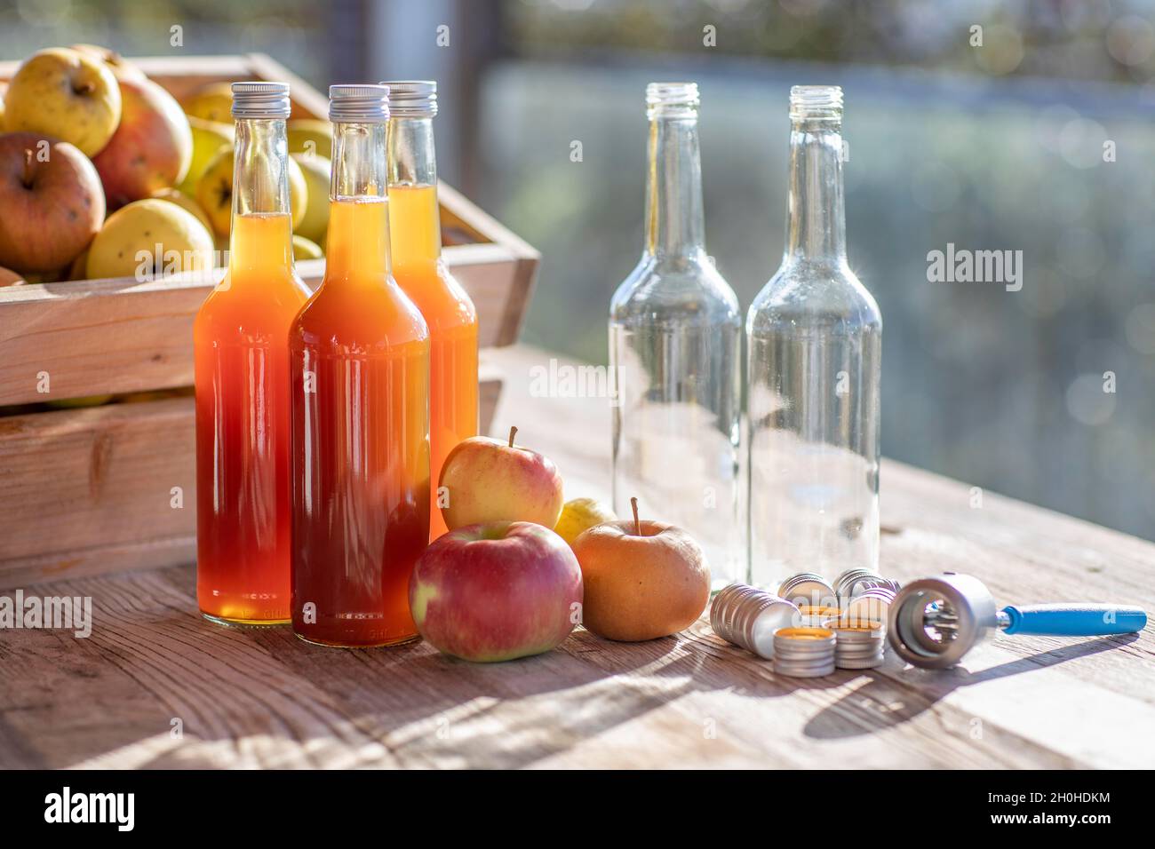 Apfelsaft natürlich trüb, hausgemacht in Saftflasche vor Äpfeln in Apfelkiste und Schraubverschlüsse mit Handkapseln Stockfoto