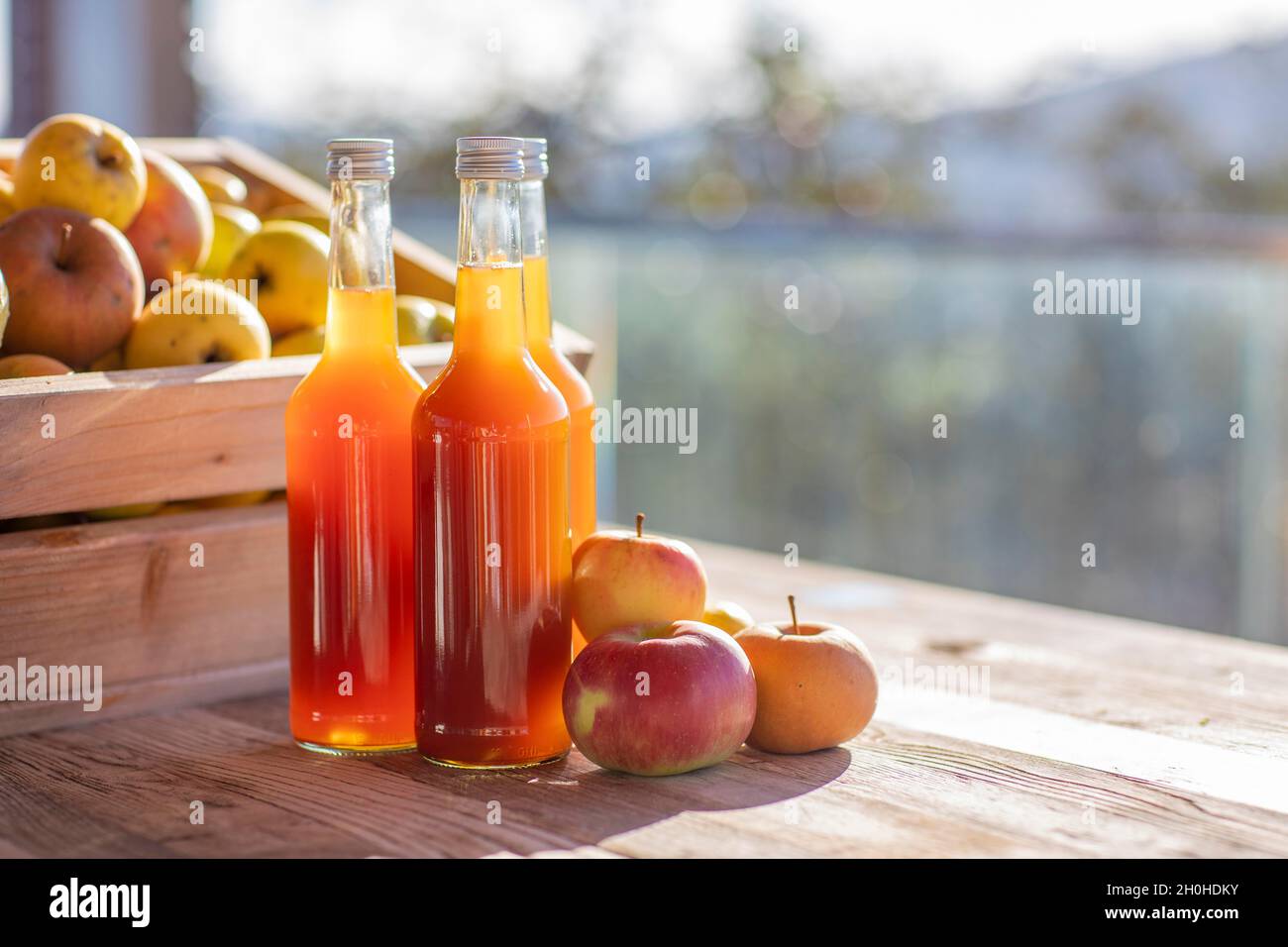 Apfelsaft natürlich trüb, hausgemacht in Saftflasche vor Äpfeln in Apfelkiste und Schraubverschlüsse mit Handkapseln Stockfoto