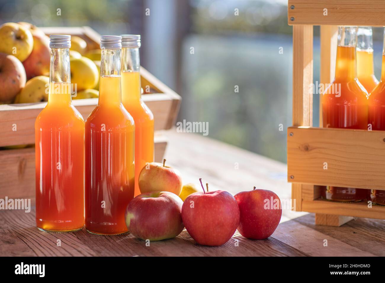 Apfelsaft natürlich trüb, hausgemacht in Saftflasche mit Äpfeln in Apfelkiste mit Herbstlicht Stockfoto