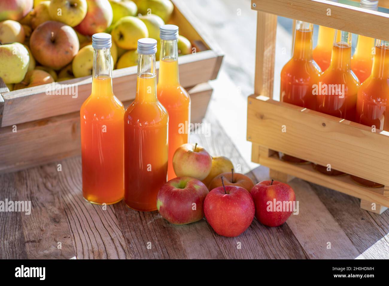 Apfelsaft natürlich trüb, hausgemacht in Saftflasche mit Äpfeln in Apfelkiste mit Herbstlicht Stockfoto