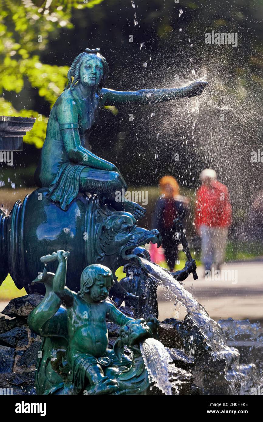 Nymphe, Drache, Wasserspeier, Putto, Kinderfigur mit Keule, Reiten, Neptun-Brunnen mit Figuren aus der griechischen Mythologie, hinter Spaziergänger, städtisch Stockfoto