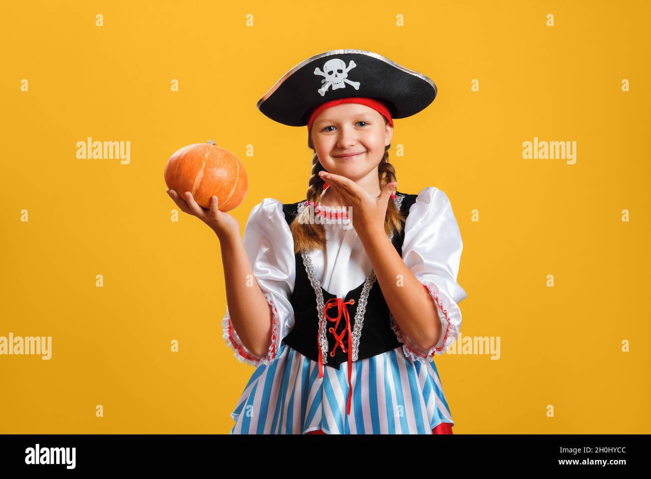 Halloween. Fröhliches Mädchen im Karnevalskostüm eines Piraten im Studio auf gelbem Hintergrund. Das Kind hält einen orangefarbenen Kürbis. Stockfoto