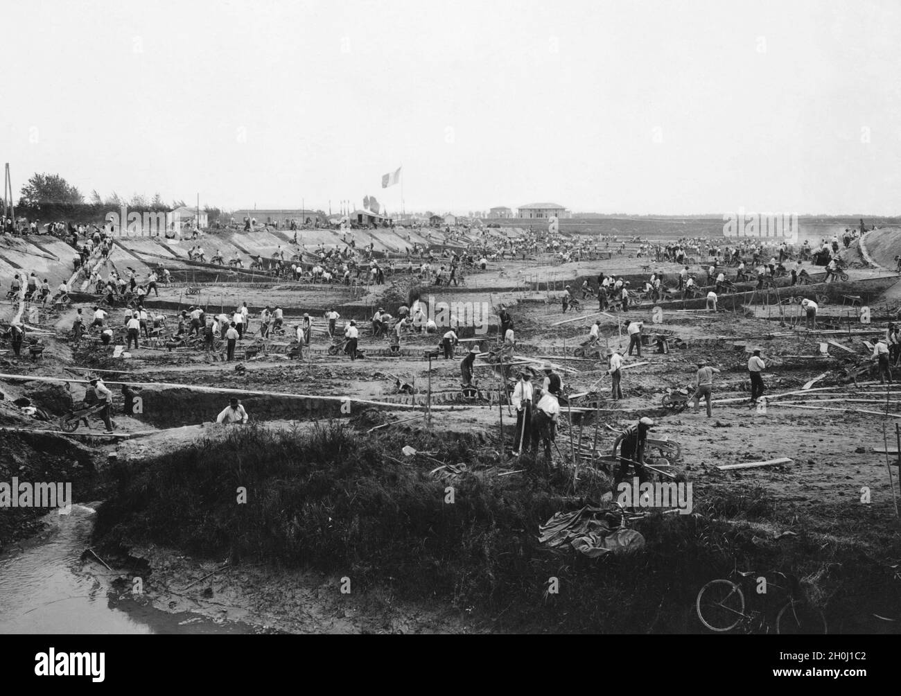 Hunderte von Arbeitern bauen im Mai 1930 in der Region Emilia-Romagna zwischen Modena und Ferrara einen Bewässerungskanal für die Landwirtschaft. Die Bauarbeiter tragen das ausgegrabene Material mit Schubkarren über Rampen weg. Die Baustellen waren eine der Maßnahmen des faschistischen Regimes in Italien, um die Arbeitslosigkeit während der Großen Depression zu bekämpfen. [Automatisierte Übersetzung] Stockfoto