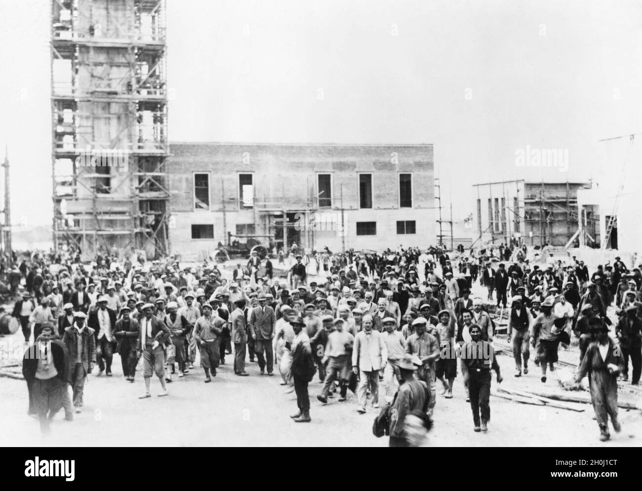 Die Stadt Sabaudia war die zweite Neugründung auf dem Gebiet der entwässerten Pontinischen Sümpfe und wurde am 15. April 1934 von Mussolini eingeweiht. Auf dem Foto, das vor der Einweihung aufgenommen wurde, überqueren zahlreiche Arbeiter die Piazza del Comune der neuen Gemeinde, im Hintergrund sieht man das Rathaus mit dem Torre Civica, beide noch im Bau. [Automatisierte Übersetzung] Stockfoto