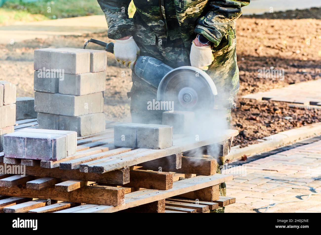 Ein Arbeiter mit einer Kreissäge schneidet in Nahaufnahme Pflasterplatten. Stockfoto