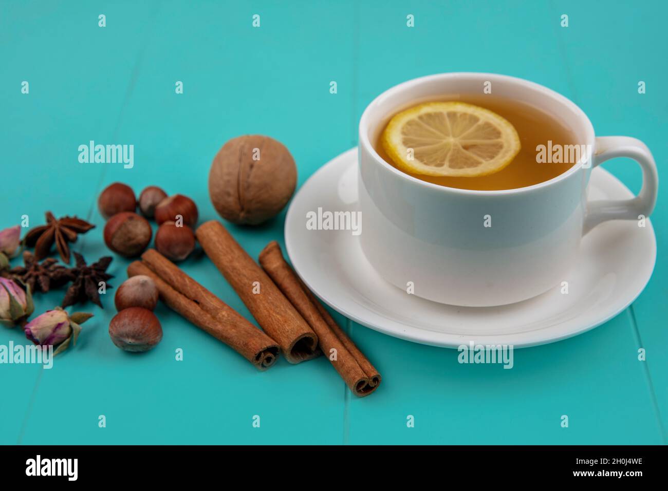 Seitenansicht einer Tasse Tee mit Zitronenscheibe und Zimt mit Nusskernen und Blumen auf blauem Hintergrund Stockfoto