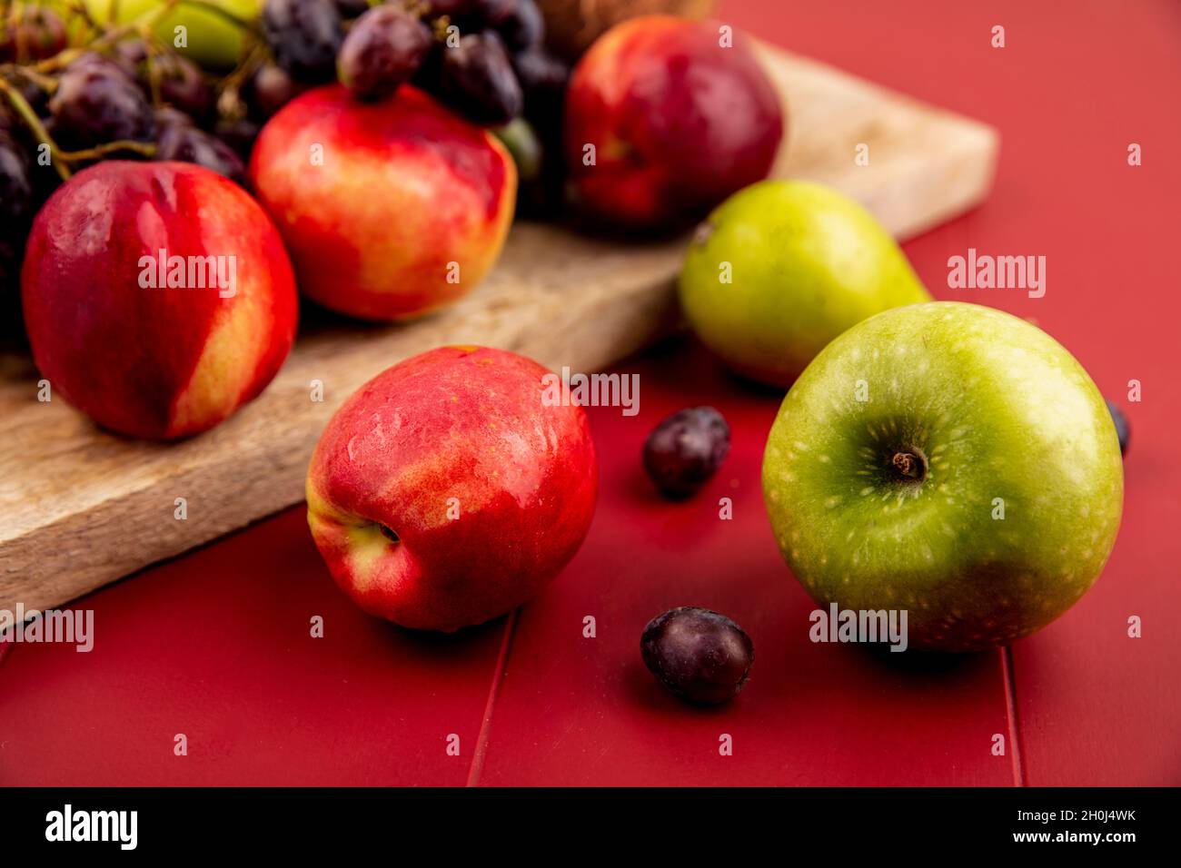 Seitenansicht von frischen Früchten wie Pfirsich auf einem hölzernen Küchentafel auf rotem Hintergrund Stockfoto