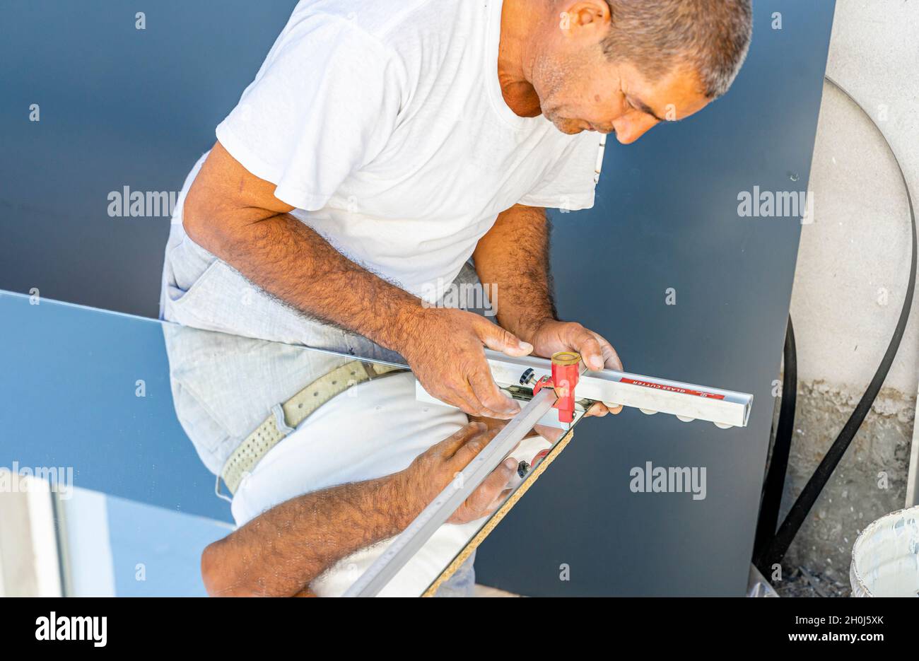 Ein Mann, der Spiegelglas mit Glasschneider schneidet, um es in der lokalen Möbelproduktion zu verwenden Stockfoto