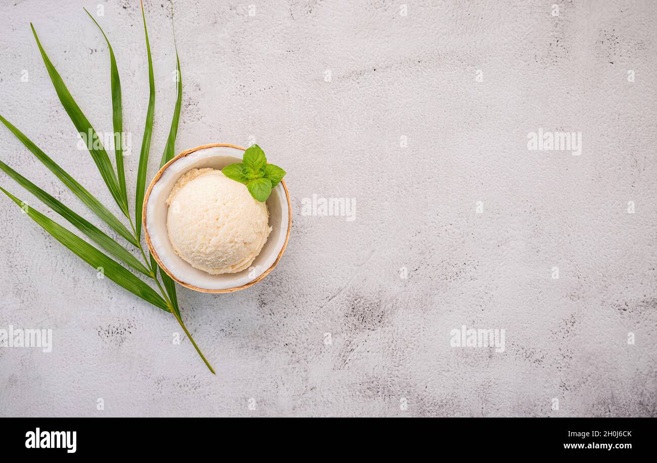 Kokoseis Aromen in der Hälfte der Kokosnuss Setup auf weißem Stein Hintergrund. Sommer und Süße Menükonzept. Stockfoto