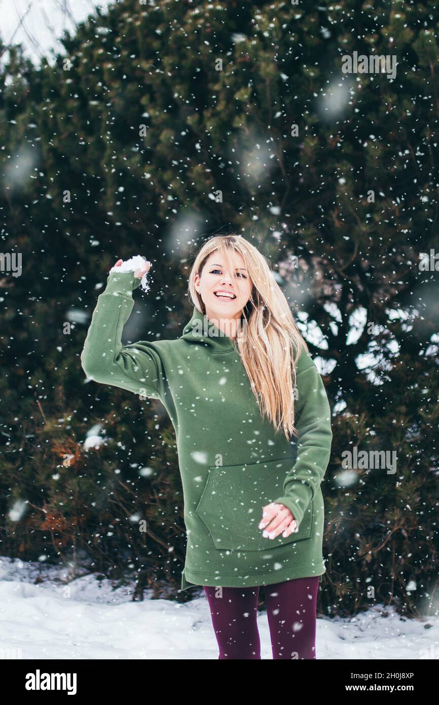 Die blonde lachende Frau wirft einen Schneeball auf die Kamera, während sie im Winter draußen spielt Stockfoto