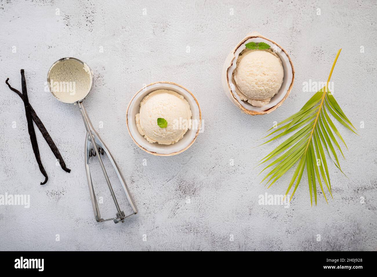Kokoseis Aromen in der Hälfte der Kokosnuss Setup auf weißem Stein Hintergrund. Sommer und Süße Menükonzept. Stockfoto