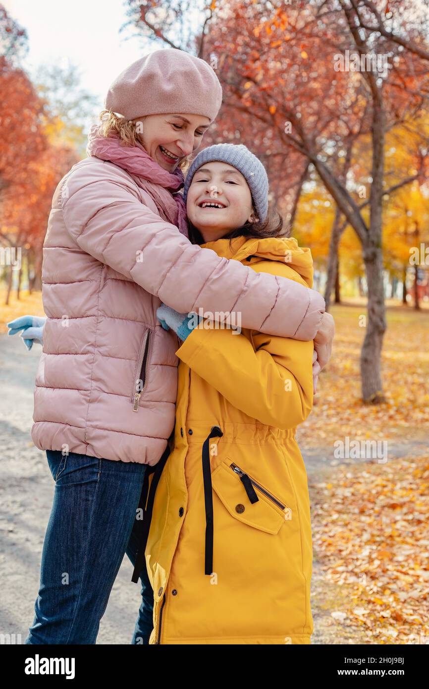Positiv lächelnde glückliche Mutter mit ihrer Tochter verbringen Zeit zusammen im Herbstpark. Mutter umarmt ihre Tochter. Herbstsonniger Tag. Gesunde glückliche Familie und Stockfoto