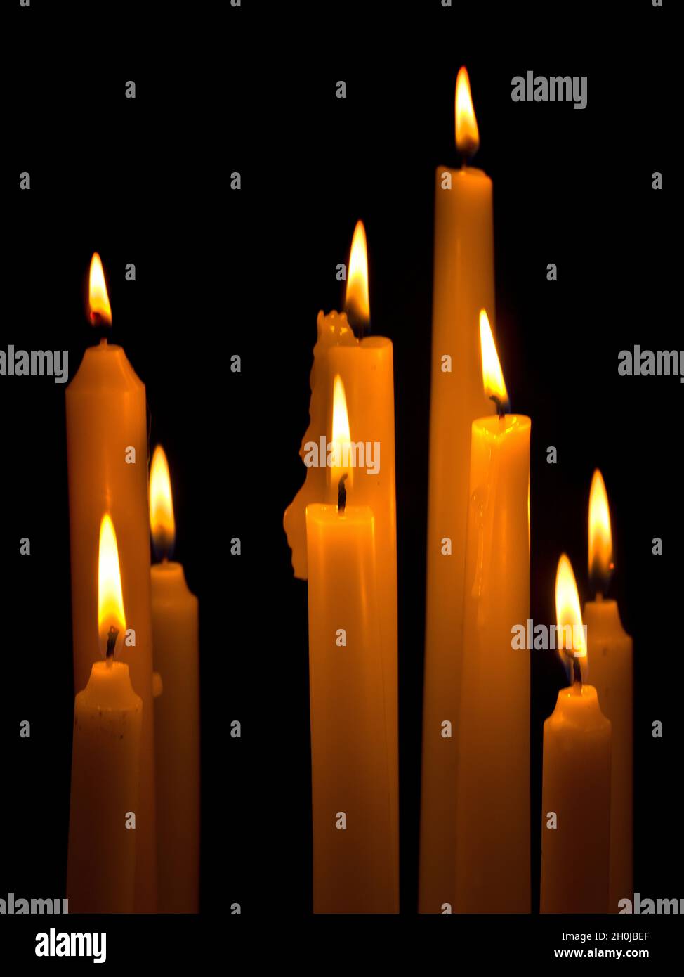 Reihe von weißen brennenden Kirchenkerzen vor schwarzem Hintergrund Stockfoto