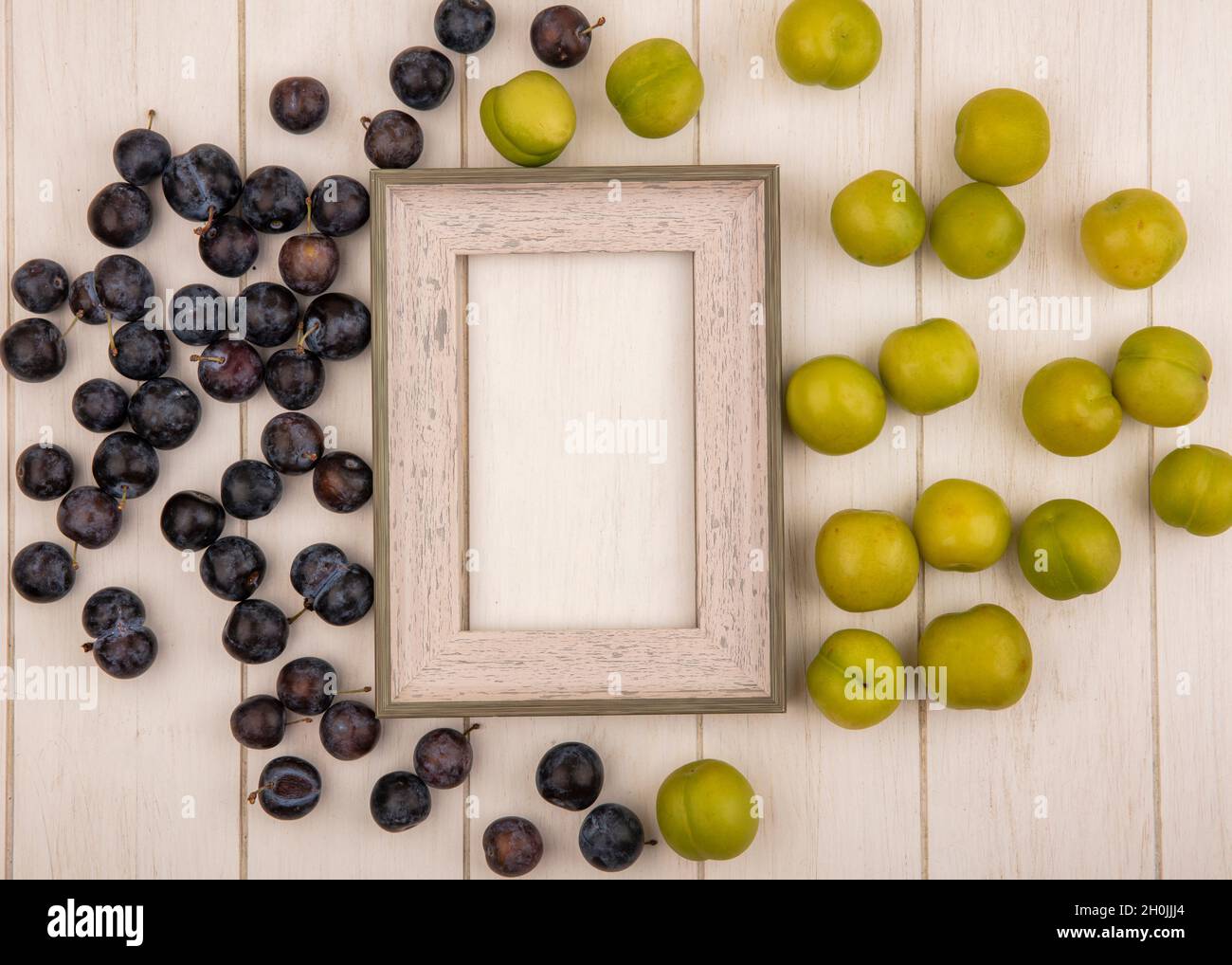 Draufsicht auf die kleinen sauer blau-schwarzen Fruchtfaul und die grünen Kirschpflaumen isoliert auf einem weißen Holzhintergrund mit Kopierraum Stockfoto