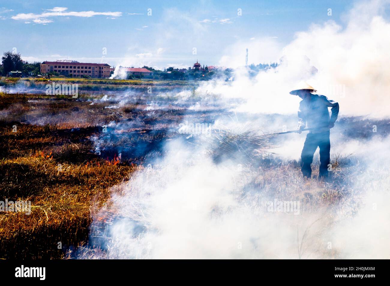 Reisfarmer steht nach der Reisernte mitten in Rauch und Feuer auf seinem Feld Stockfoto