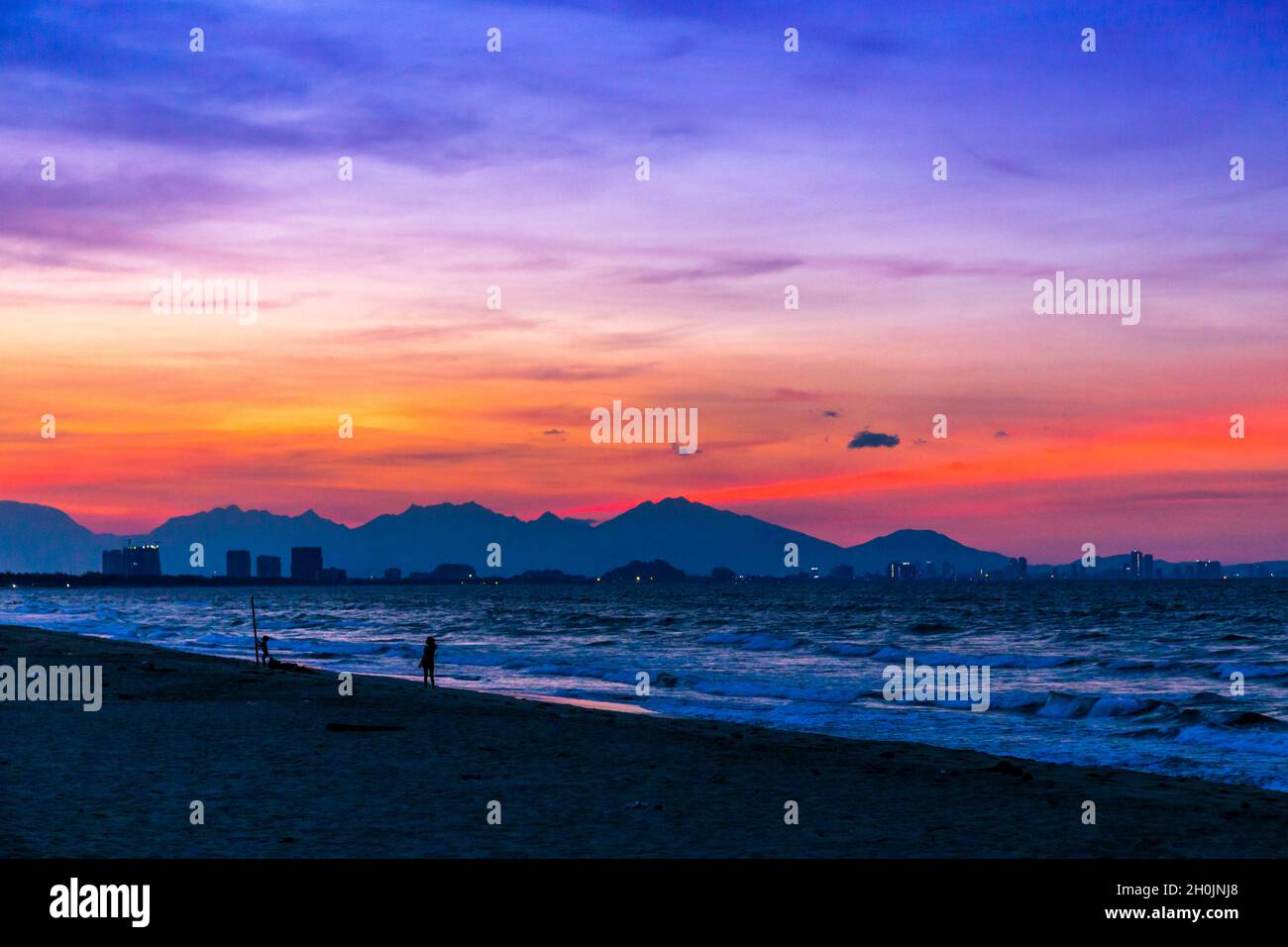Wunderschöner Sonnenuntergang am Strand mit Rot-, Blau- und Magentaroten, mit dem Ozean und den Bergen in der Szene. Stockfoto
