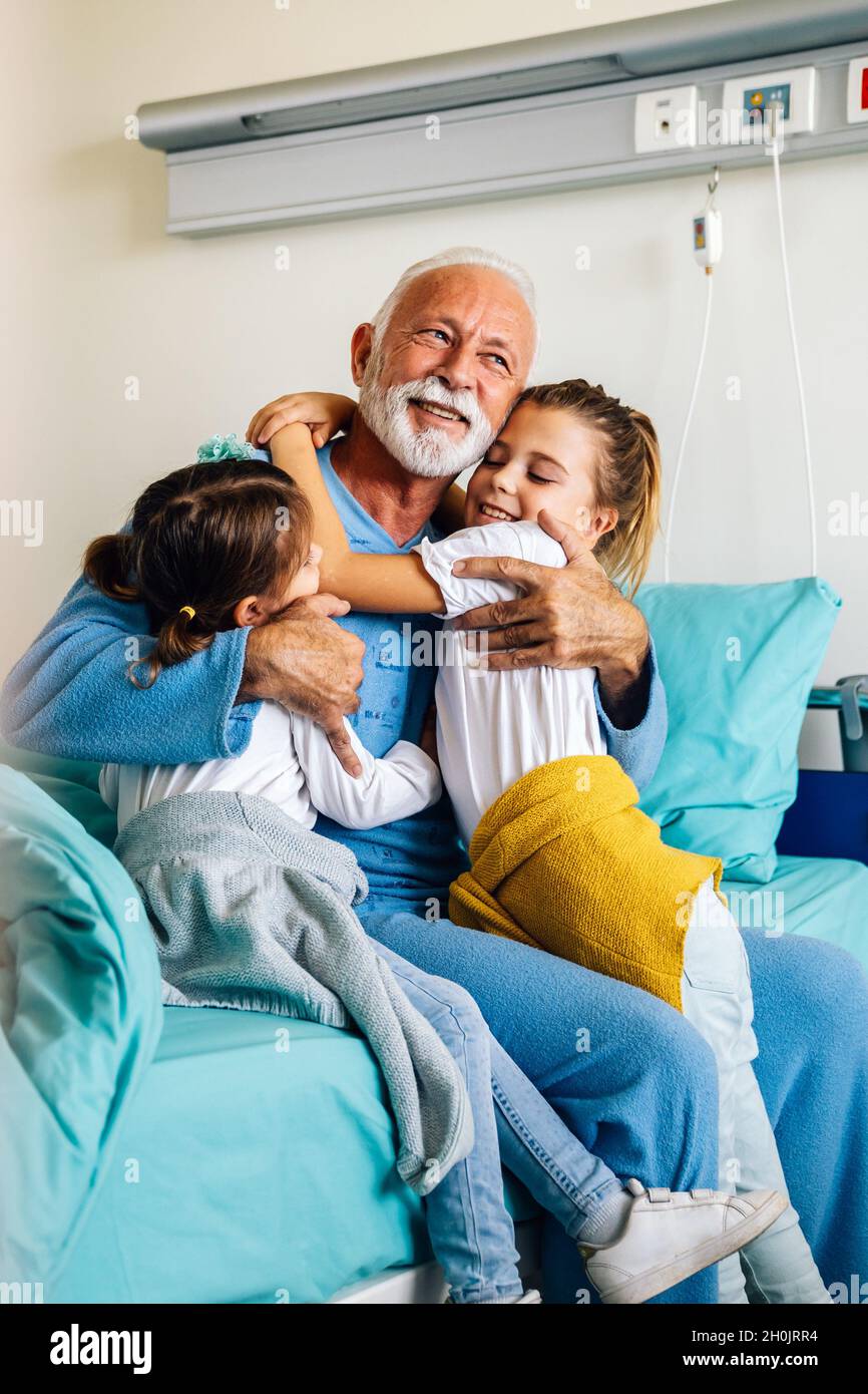 Glückliche Enkelkinder, die Großvater auf der Krankenhausstation besuchen. Support-, Familien- und Gesundheitskonzept. Stockfoto