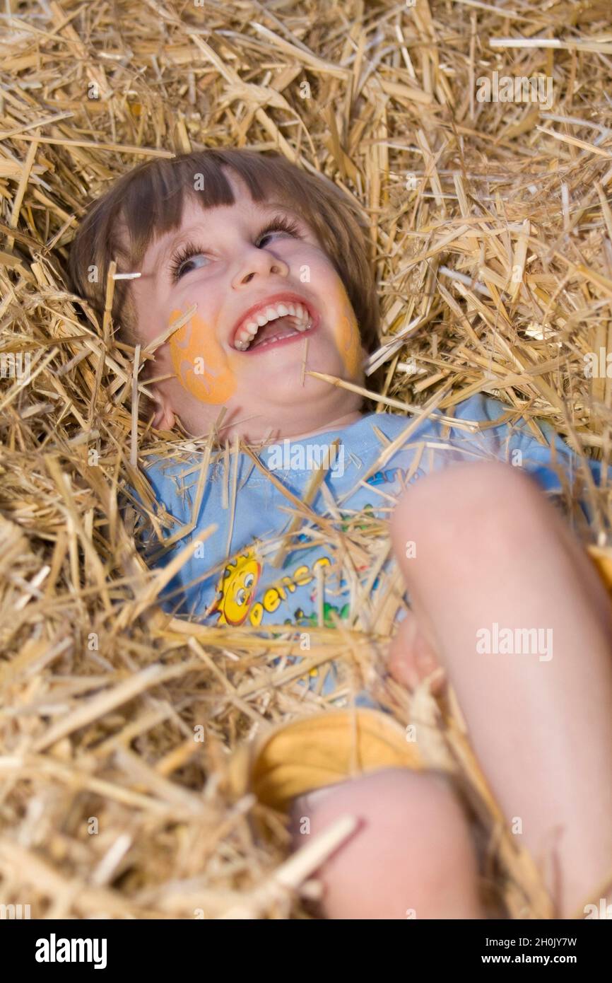 Der kleine Junge liegt lachend im Stroh Stockfoto