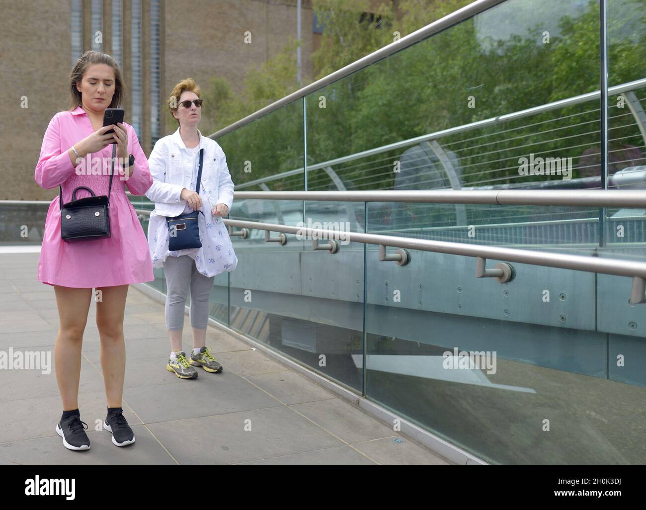 London, England, Großbritannien. Frau, die ihr Mobiltelefon auf der Millennium Bridge anschaut Stockfoto